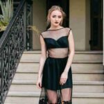 Woman wearing a stylish party wear dress in black with sheer mesh design, posing on outdoor stairs.