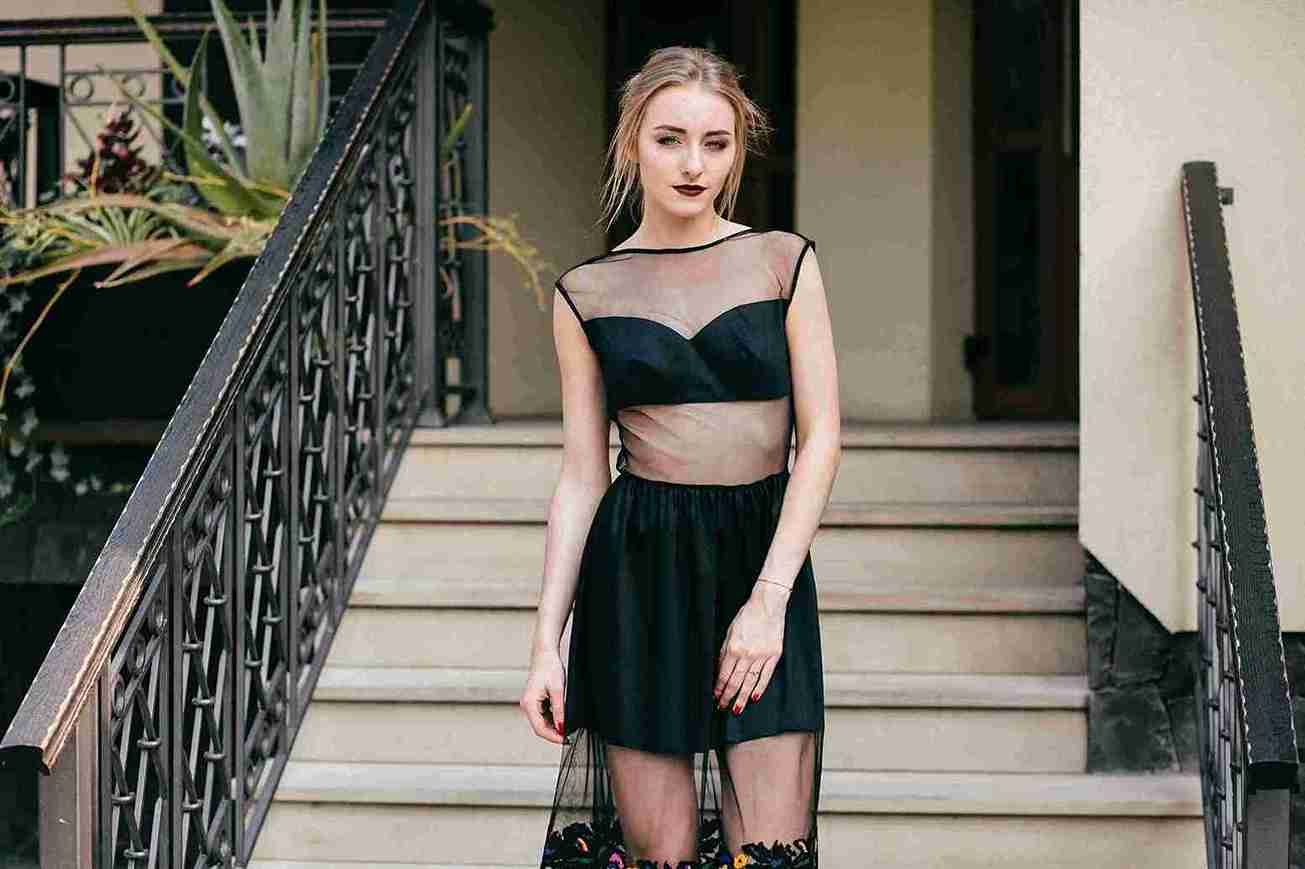 Woman wearing a stylish party wear dress in black with sheer mesh design, posing on outdoor stairs.