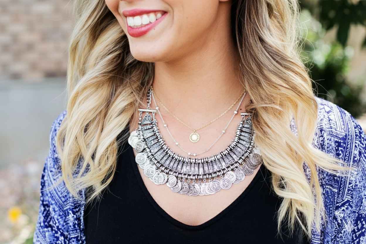 Close-up of a woman demonstrating how to layer necklaces by mixing a chunky silver coin choker with delicate gold chains.
